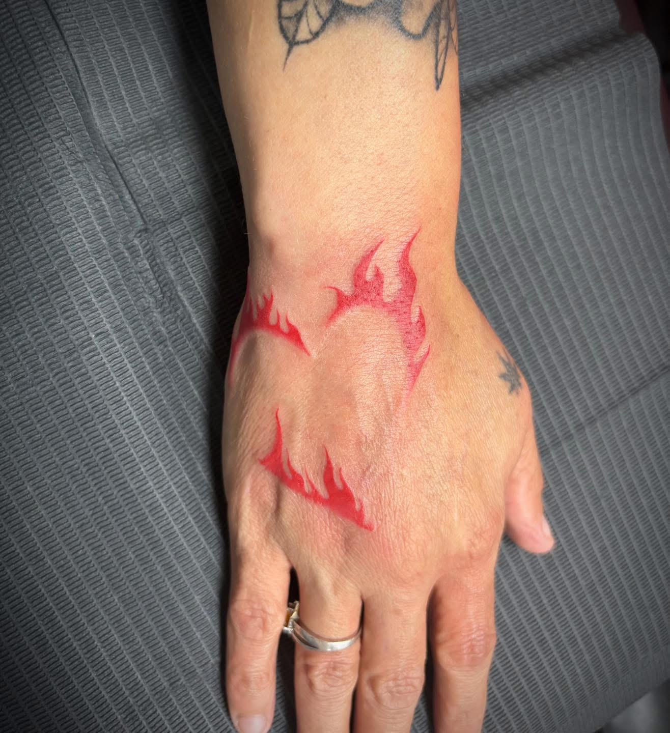 Red ink flame heart tattoo on a hand