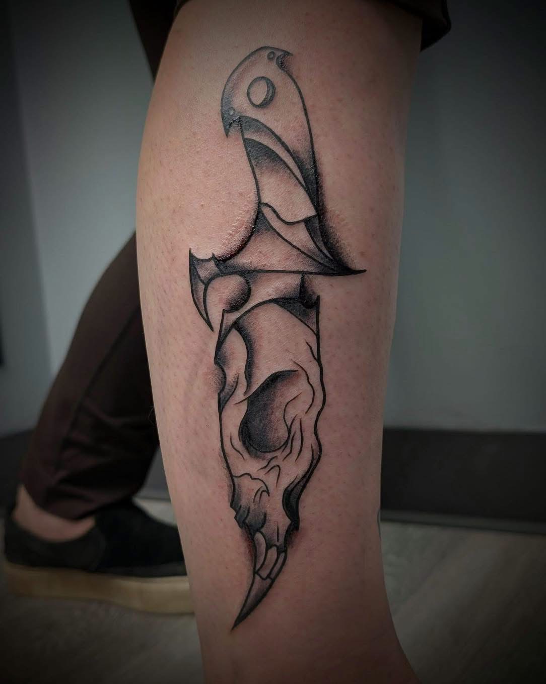 Blackwork raven skull and dagger tattoo on a calf