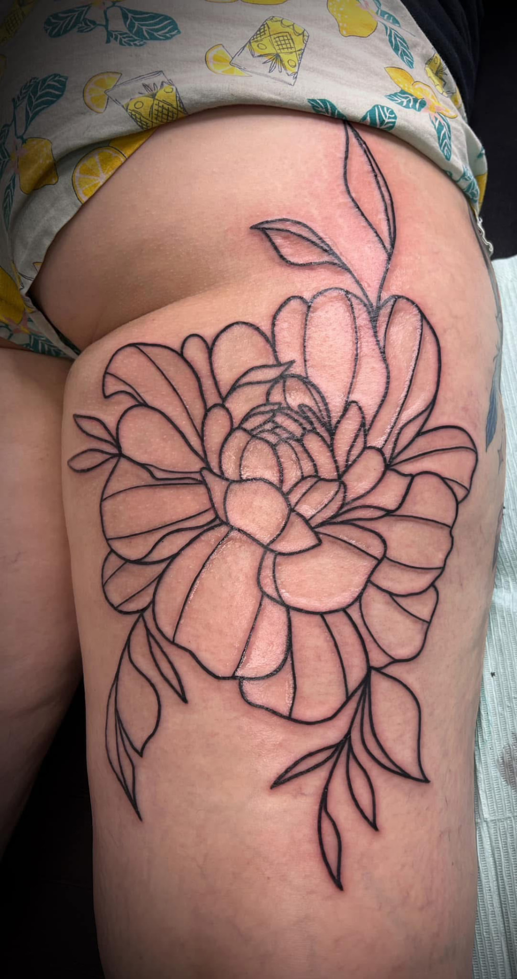 Fine-line peony outline tattoo on a hip