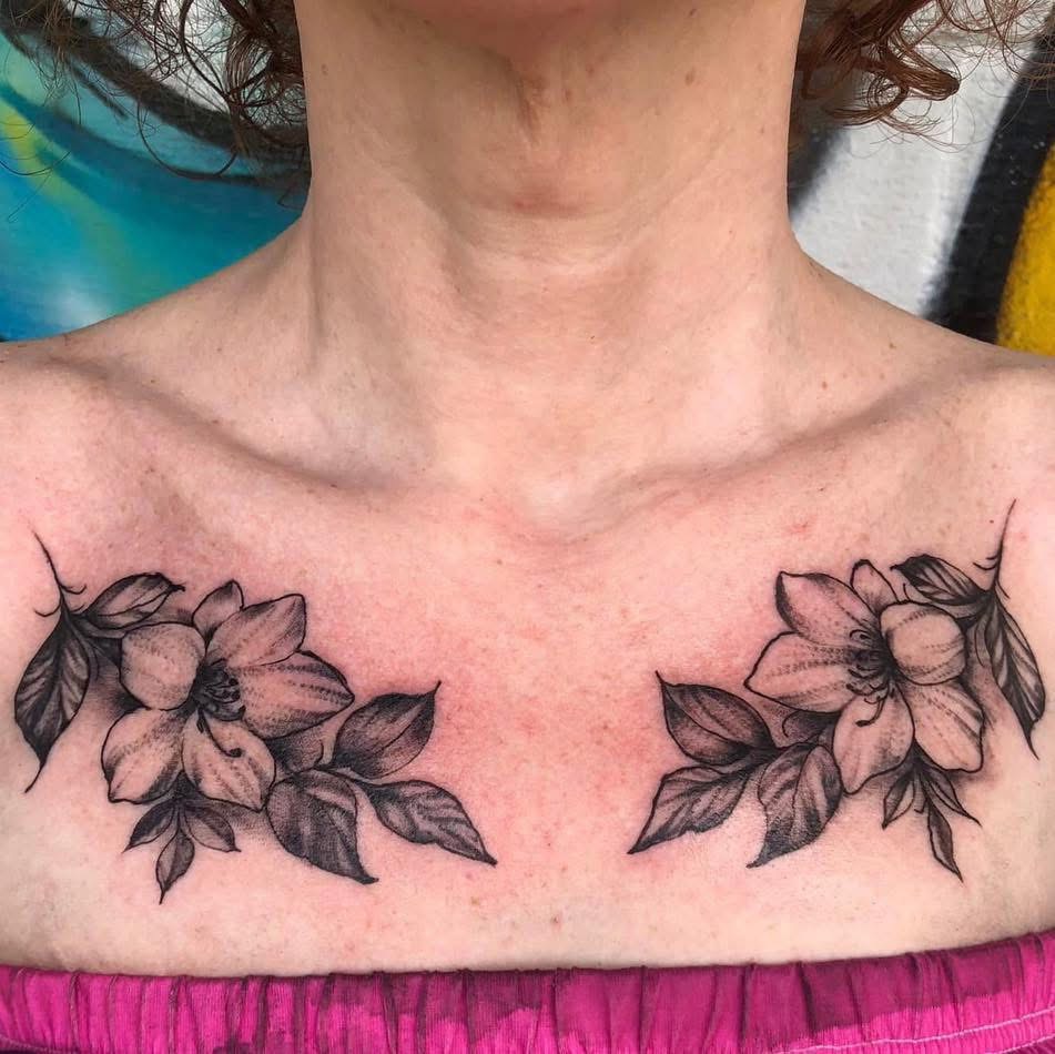 Fine-line black and grey lilies across the collarbones