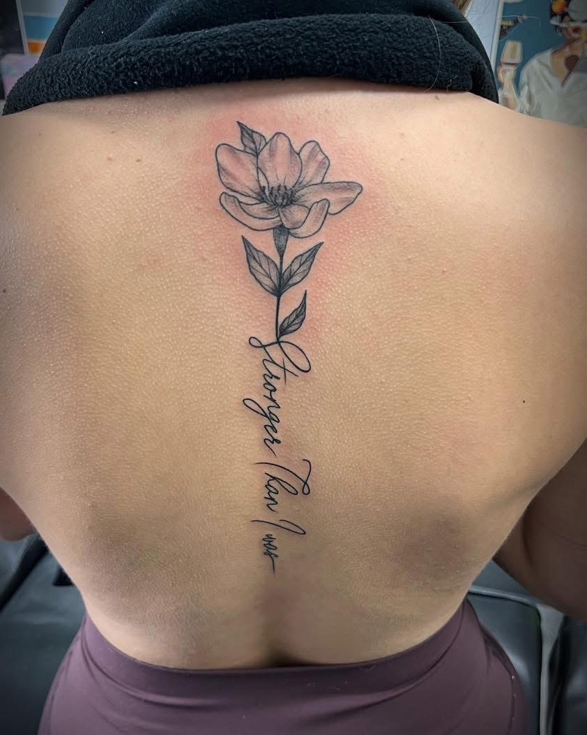 Fine-line magnolia with stronger than him script down the spine